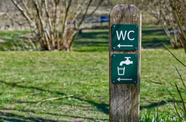 WC ve su musluğu sembolleri olan bir parktaki tahta tabela, Danimarka 'da Kollung yakınlarında kurulanacak WC tuvaleti ve ferah su yönlerini gösteriyor.