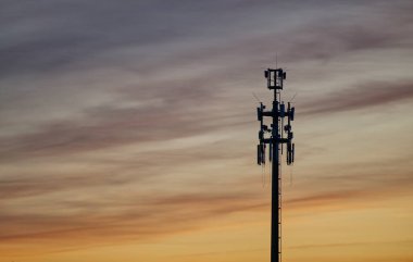 Gün batımında Hamburg 'da LTE UMTS ve mobil internet için bir radyo kulesi altın ve mavi-gri renklerin arka planına karşı. Antenlerden kablolar sarkıyor.