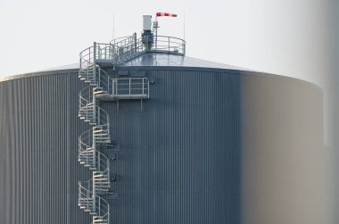 Danimarka 'nın Kvaers kentindeki biyogaz sahasının BIO benzin deposunun detayları da büyük siyah fıçı şeklinde bir depo, ön tarafında uzun ve yüksek döner bir merdiven var.