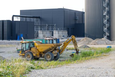 Danimarka 'nın Kvaers kentindeki BIOGas depolama alanında büyük siyah binalar ve fıçı şeklinde depolama tankları olan bir inşaat aracının görüntüsü