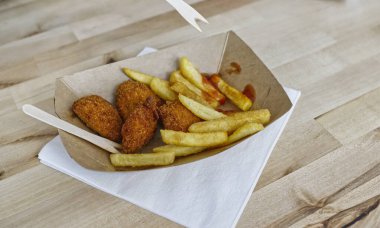 Ekolojik kartondan yapılmış kahverengi bir kâse içinde ahşap çatalla yenmemiş bir patates kızartması. Ayrıca içinde kızarmış tavuk ve ketçap da var..