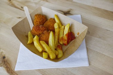 Ekolojik kartondan yapılmış kahverengi bir kâse içinde ahşap çatalla yenmemiş bir patates kızartması. Ayrıca içinde kızarmış tavuk ve ketçap da var..