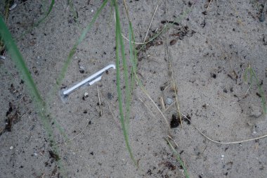 Plajda sarılı ve kullanılmamış bir saman, kum ve kir tanelerinin arasında uzanır. Çerçevenin içinde kumsal çimenleri kıvrılır..