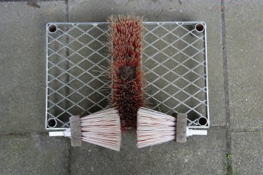 Bir sokak süpürgesinin kırmızı fırçalarının bağlandığı metal bir ızgaradan oluşan bir ayakkabı temizleme sistemi.