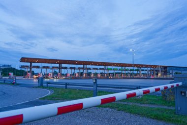 Danimarka 'nın Korsor Kursoer kentinin doğu yakasındaki Öresund Oeresund Köprüsü' ndeki gişe bariyerlerinin önünde alacakaranlıkta geniş görüşlü kırmızı ve beyaz bir bariyer bulunuyor.