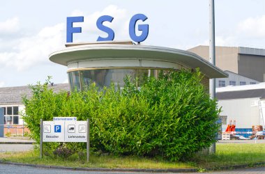 FSG tersanesinin resepsiyonunun olduğu giriş alanı ve arka planda vinç olan Batteriestrasse 'deki Flensburg tabelasını.