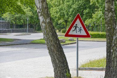 Sessiz bir yolda ağaçların yanında yaya geçidi işareti var..
