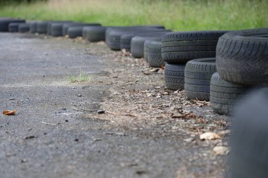 Eski lastikler eskimiş asfalt bir yolda dizilmiş ve arka planda çimenler var..