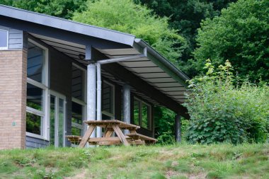 Geniş pencereli, dışarıda piknik masası olan, yemyeşil bir bina..