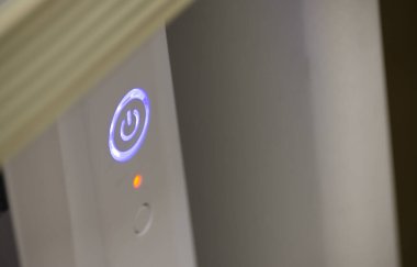 Elektronik bir cihazda parlayan bir güç düğmesi, açık olduğunu gösteren mavi bir LED ışığı ve altında küçük bir kırmızı ışık var..