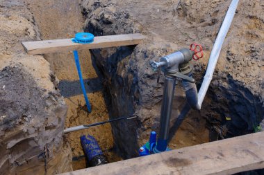 Bantla sarılmış bir su borusuna ulaşmak için derin bir çukur kazılır. Hortum, yakınlardaki bir vanaya bağlıdır. Kırmızı uyarı bandı yere saçıldı..