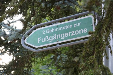 Soldaki kutup noktalarına metal bir ok işareti asılmış. Bu da yaya bölgesine 2 dakikalık yürüyüş mesafesini gösteriyor. Metin Almanca, kentsel bir ortamda yaya trafiği için net yönler sağlıyor.