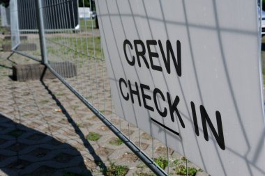 Metal bir ağ çitinde siyah harflerle beyaz bir işaret var. Bir yaz günü asfalt kiremitler arasında yeşil çimenler büyür..