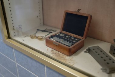 Esmer, eski metal diş eklentileriyle dolu bir kutu. Bitleri deliyor. Tıbbi makas şişeleri kalın tozla kaplı.