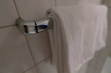 Banyonun duvarına beyaz bir havlu askısı asılır. Beyaz fayanslardan oluşan bir zemine karşı duruyor. Eklemlerden biri hafifçe kırılmış görünüyor, bağlantıda gözle görülür bir ayrılık var..