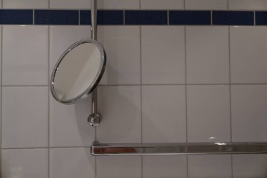 Modern erişilebilir duş alanı yatay ve dikey metal tutma çubukları, ayakta duran duş aynası, hepsi dekoratif mavi şeritli beyaz fayanslara karşı.