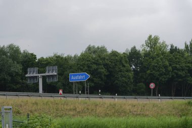 Mavi bir Ausfahrt çıkış levhası ve yolun sağ tarafında saatte 60 kilometre hız sınırı işareti olan bir Alman otobanı mesafesi..