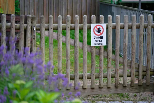 Ahşap bir giriş kapısında sadece Almanca imzalı bir personel var. Yaban çiçekleri ve otlarla çevrili olan bölge, huzurlu bir kırsal alanda özel bir alanı işaret ediyor..