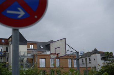 Paslı bir basketbol sahasının yanında geniş bir park yeri tabelası yok. Arka planda, eski iki ve üç katlı binalar görülebiliyor..