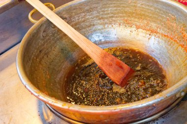 Derin alüminyum bir tencerede kaynamış kahverengi karışımı karıştıran ahşap bir spatula bulunur. Tencere ateşte, muhtemelen Kopenhag CPH 'de geleneksel yağlı bir tabak pişiriyor.