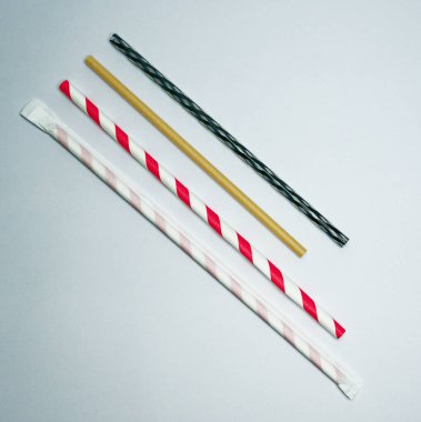 Beyaz arka planda dört adet kağıt, plastik ve kartondan yapılmış pipet ve bir adet siyah ve yeşil çizgili plastik pipet uzanıyor..