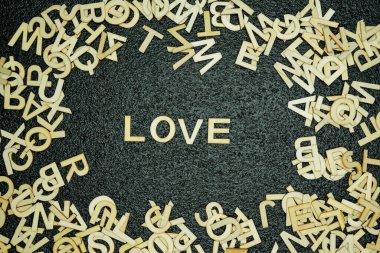 Aşk kelimesi siyah kauçuk bir paspasın ortasında tahta harflerle hecelenirken diğer ahşap harfler etrafa saçılmış oyuncu ve sanatsal bir sahne yaratıyor..