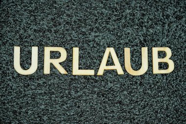 Almancayı hecelemek için düzenlenmiş tahta harfler net bir şekilde siyah bir arkaplanda uzanır. Tatil ya da tatili minimalist bir şekilde sembolize eder..