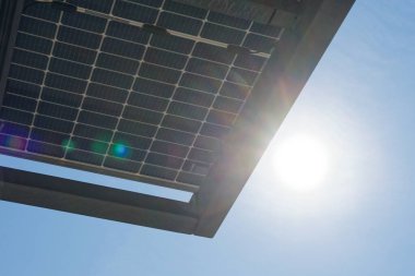 Parlak güneş ışığı ve mavi gökyüzü altında güneş panelleri olan metal yapı. Görüntü, elektrikli arabalar için şarj istasyonu için temiz enerji üretimini gösteriyor.