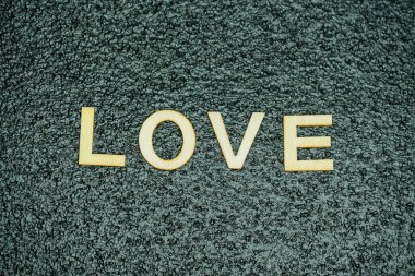 Aşk kelimesi siyah kauçuk bir hasırın üzerine yerleştirilmiş ahşap harflerle şekillenir. İnce bir dokunuşla, düzgün ve yaratıcı bir görsel sunum sunar..