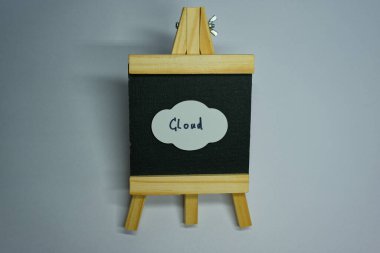 Ahşap bir tezgah, üzerine kağıt bulut yapıştırılmış küçük siyah bir kumaş ekran tutar. Bulutta CLOUD kelimesi işaretli, dijital ya da yaratıcı temaları sembolize ediyor..
