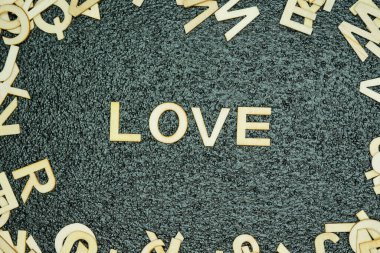 Ahşap harfler siyah kauçuk bir hasırda aşk kelimesini oluşturur. Etrafı dağınık ahşap harflerle çevrilidir. Yaratıcı ve dinamik bir kompozisyon yaratır..