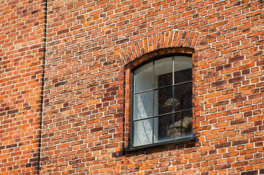 Klasik bir bronz Roma heykeli, kırmızı tuğla bir duvarın kırsal ahşap çerçeveli penceresinde duruyor. Eski heykel, eski binanın tarihi mimarisine ebedi bir cazibe katıyor..