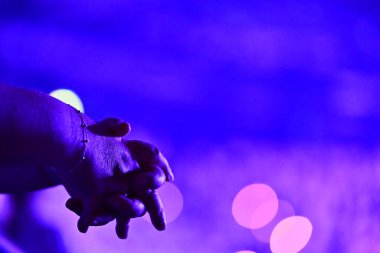 İki kadın el ele tutuşuyor. Bir bileğinde hassas bir bilezik var. Arkaplan parlak pembe ve mor neonlarla parıldıyor, birliği, sıcaklığı ve nazik duyguyu simgeliyor..