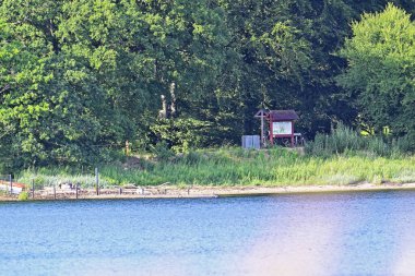 Manzaralı bir sahil sahnesi otlak kıyı şeritlerini ve bölge hakkında bilgilendirme işaretleri olan küçük bir kulübeyi gösteriyor. Yakınlarda birkaç bisiklet park edilmiş ve deniz kenarındaki atmosfere huzur katıyor..