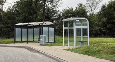 Halka açık iki durak yan yana duruyor. Biri bankı ve çöp tenekesi olan cam ve beyaz metal bir otobüs durağı; diğeri ise bisikletler veya küçük araçlar için siyah metal bir sığınak..