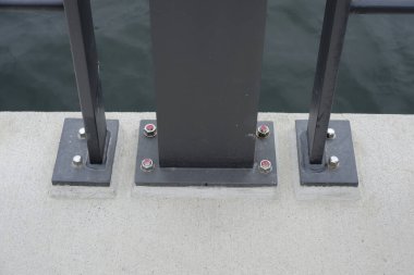 Beton bir yüzey, geniş cıvatalarla korunan birkaç siyah metal direği barındırır. Arkalarında su görünüyor. Bu da Flensburg batı yakasında bir rıhtım ya da iskele olduğunu gösteriyor.