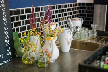 Antika çaydanlıklar ve tezgahın üzerine konmuş klasik beyaz çaydanlıklar arka planda, görünen bir metal musluk ve diğer beyaz seramik bulaşık takımları düzgünce düzenlenmiş mutfak alanının bir kısmını ortaya çıkarıyor..