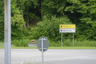 Asfaltlı bir yolda iki yön işareti vardır. Üstteki sarı işaret Pattburg 'a beş kilometre uzaklıktayken, alttaki beyaz işaret bir gemi ikonu ve Harrislee' nin Almanca metnini gösteriyor..