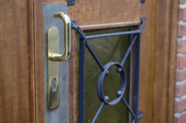 Cilalı ahşap bir kırmızı kapı dekoratif siyah metal ızgara ile süslenmiş küçük sarı bir cam panele sahiptir. Altın bir kol zarif giriş tasarımını tamamlar..