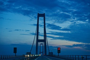 Oresund Oeresund Köprüsü, limanı ikiz at arabaları ve merkezi bir bariyerle kaplar. Yan ekranlar bir rüzgar simgesi gösterirken, açık akşam gökyüzü araçlar ve şehir yolculuğu için sakin bir zemin oluşturuyor.