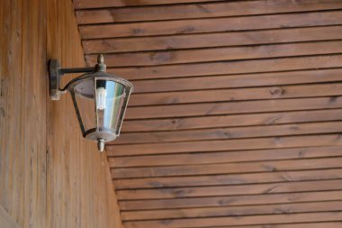 Kırsal ahşap bir duvar tavanı ve zemin çerçevesi içinde modern bir ampul bulunan metal bir fener. Eski cazibe ve yeni hizmet karışımı sıcak ve benzersiz bir atmosfer yaratır..