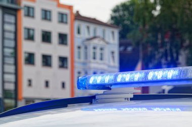 Flensburg Almanya 'sında etkin mavi fener ışıklarına sahip bir polis aracının çatısı, şehir güvenliğini ve emniyet güçlerini simgeleyen geleneksel Alman evlerinin arka planına sahip..