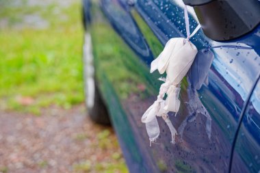 Yan aynasında beyaz bir fiyonk bulunan koyu mavi bir araba, yeni bir düğün kutlamasını sembolize ediyor. Parlak yüzey çevreyi yansıtıyor, zarafet ve şenlik katıyor..