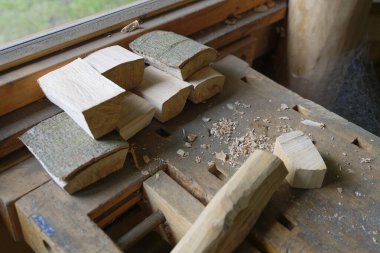 Katı montlu tahta mengene pürüzsüz yuvarlak bir dalı kavrar, kabuğu düzgünce kaldırılır. Yakınlarda küçük tahtalar ve çipler var. Basit bir açık hava düzeninde dikkatli bir el işi ve hobi olarak ahşap işçiliği öneriliyor..