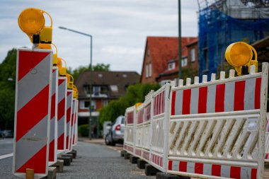 Kırmızı çizgili ve uyarı lambalı beyaz plastik bariyer iskele ve güvenlik ağının yanında yolu kapatıyor. Bakım devam ederken fazladan dikdörtgen işaretler erişimi kısıtlıyor.