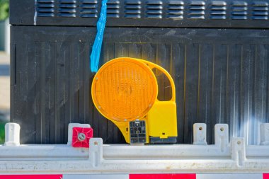 Mevzilenmeden önce depoda birkaç plastik bariyer yan yana duruyor. Kırmızı bantlı beyaz paneller ve kehribar yansıtıcılar kaldırımda dinleniyor. Sokaktaki bakım işleri için şeritleri kapatmaya hazırlar..