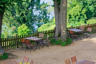 Ahşap bir çitin yanında bir ağacın altında iki masa, bira bardakları ve geride bırakılmış küçük bir fincan. Vadideki mavi deniz korkulukların ardında ziyaretçiler gittikten sonra sessiz bir duraksama devam ediyor..