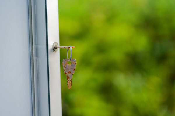 Металлический ключ сидит в белом оконном замке, в то время как другой висит на маленьком кольце. Оба окрашены ржавчиной и коричневыми пятнами, намекая на возраст, влагу, и долго неиспользуемые тихая комната