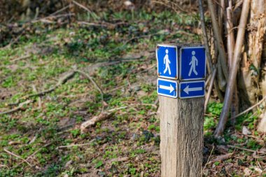 Parktaki bir levhada bir yüzü sol tarafı işaret eden bir kişi diğerini de sağ tarafı işaret eden bir ok görülüyor. Oklar neredeyse birbirlerini dengeleyecekler..