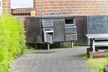 Hurdaya çıkmış bir metal mutfak atölyesi, sanki bir kafeden kaldırılmış, fırçalanmış çelik görünümlü, yıpranmış ve hurdaya hazır bir ev gibi, değişim ve yoğun çalışma saatlerinin sona erdiğini gösteren bir sokak manzarası..